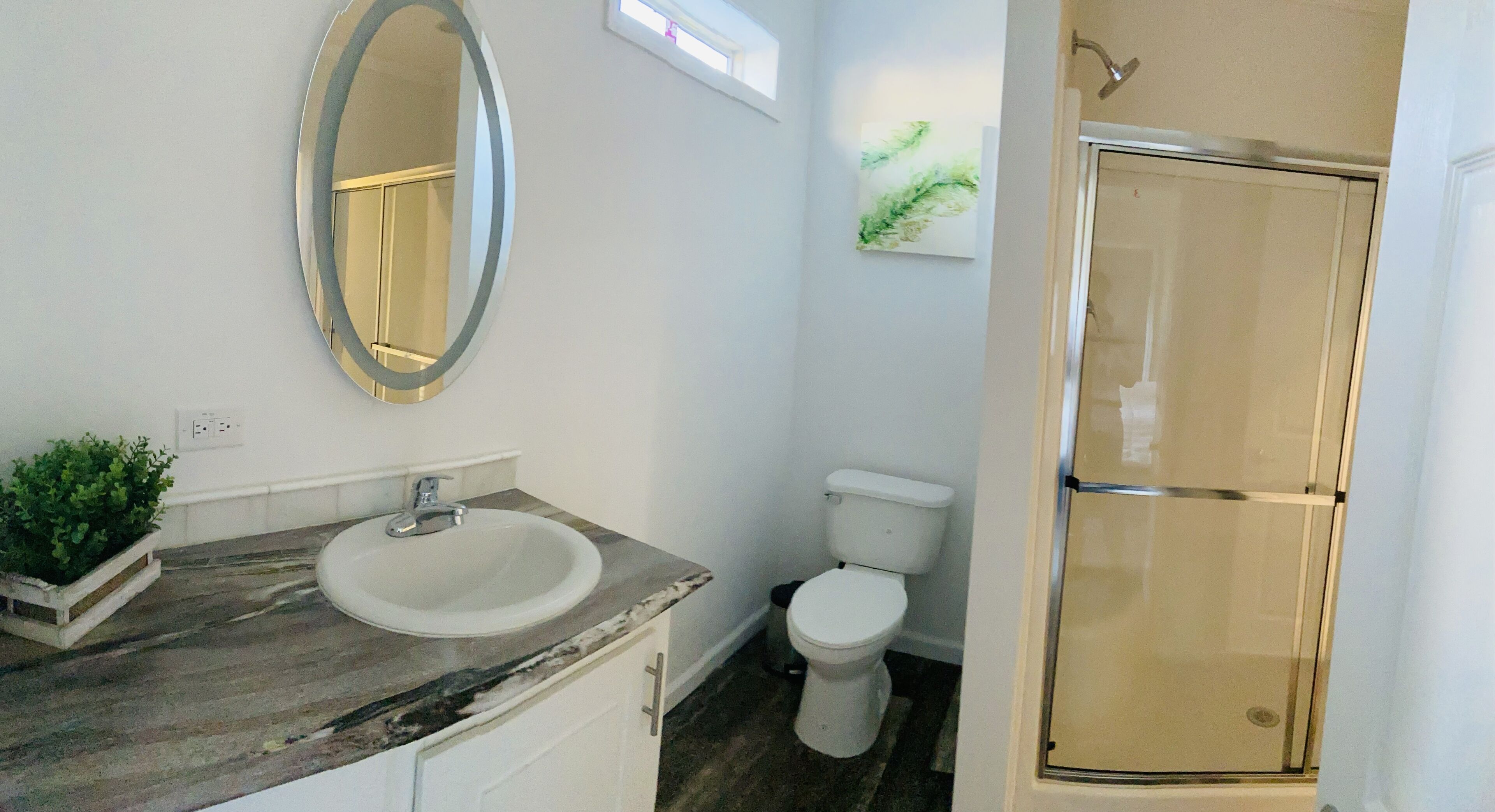Baño con lavamanos de mármol, inodoro y cabina de ducha de vidrio.