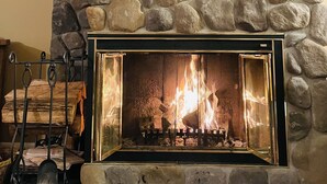 A stone fireplace with a metal screen, a wooden shelf above, and two crossed paddles on the wall.