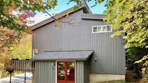 A gray wooden building with a red door and a small attached structure.