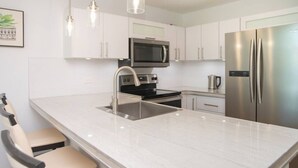 A modern kitchen with white cabinets, stainless steel appliances, a large island with a sink, and pendant lighting. - Landing View 304 with beautiful roof top terrace (Barrio Puntas, Rincón)