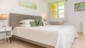 A bedroom with a bed, nightstands, a window with curtains, and wall art. - Landing View 304 with beautiful roof top terrace (Barrio Puntas, Rincón)