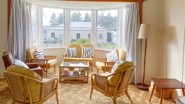 Un salon chaleureux avec un ensemble de canapés, des fauteuils, une table basse et un lampadaire. De grandes fenêtres offrent une vue sur l’extérieur.