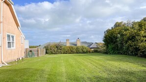 Une pelouse bien entretenue, avec un bâtiment sur la gauche et un grand arbre sur la droite.
