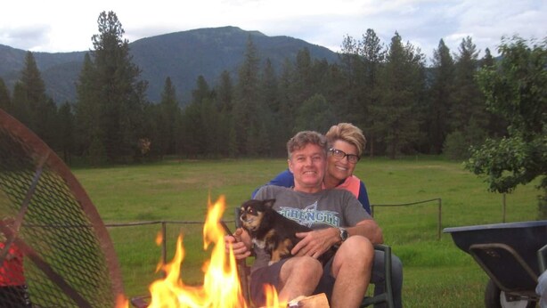Two people sitting by a campfire with a mountainous background. - Green Acres Ranch Family Style (Thompson Falls)