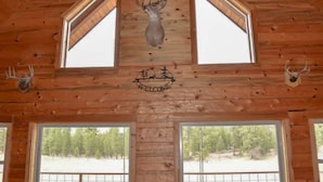 A wooden cabin interior with a deer head mounted on the ceiling, two deer antlers on the walls, and a logo with a tree and a deer. - Green Acres Ranch Family Style (Thompson Falls)
