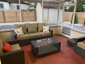 Relax in a serene outdoor space with a sofa set and wicker chairs, offering a view of the backyard.