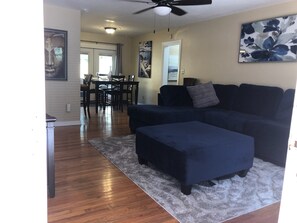 Relax in this stylish living room with a sofa, ottoman, and dining area, featuring a large abstract painting and a window with a view.
