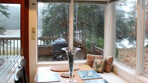 Un coin salon confortable avec une table, un vase en verre et une vue sur une terrasse et des arbres.