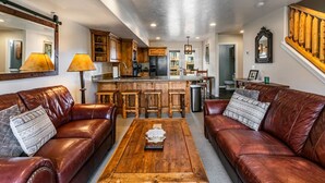 A living room with leather sofas, a wooden coffee table, and a kitchen in the background.