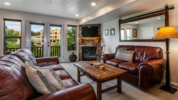 A living room with leather sofas, a fireplace, a TV mounted on the wall, and a large mirror.