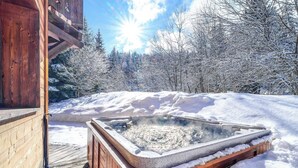 Un jacuzzi de madera rodeado de árboles cubiertos de nieve y una terraza de madera.