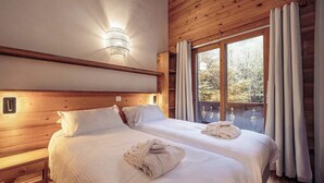 Una habitación con dos camas, cabeceros de madera, una mesita de noche, una lámpara de pared y una ventana con cortinas.