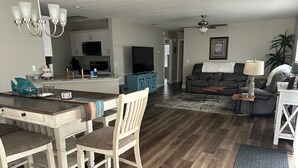 A modern living room with a grey sofa, a coffee table, and a dining area with a white table and chairs. - Modern Comfort & Prime Location in The Villages – Golf Cart Included! (The Villages)