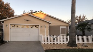 Une maison de plain-pied avec un garage, une clôture en bois peinte en blanc et une pelouse bien entretenue.