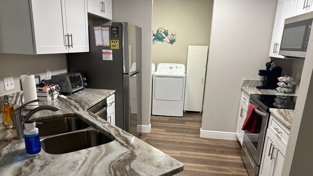 A compact kitchen with a marble countertop, stainless steel sink, and white cabinetry. - Prime Location in The Villages – Golf Cart Included and 2 King Sized Beds! (The Villages)