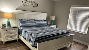A bedroom with a bed, nightstands, a wall decoration, and a window with blinds. - Modern Comfort & Prime Location in The Villages – Golf Cart Included! (The Villages)