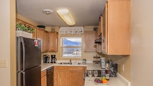 Cocina compacta con armarios de madera, un refrigerador negro, una ventana con vistas y una encimera con una copa de vino y fruta.