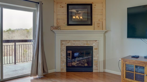 Una sala de estar con chimenea, televisor montado y balcón con vista al paisaje.