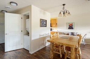 Un comedor con una mesa y sillas de madera, una cocina al fondo y una lámpara en el techo.