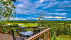 A deck with outdoor furniture overlooking a forested landscape and distant mountains.