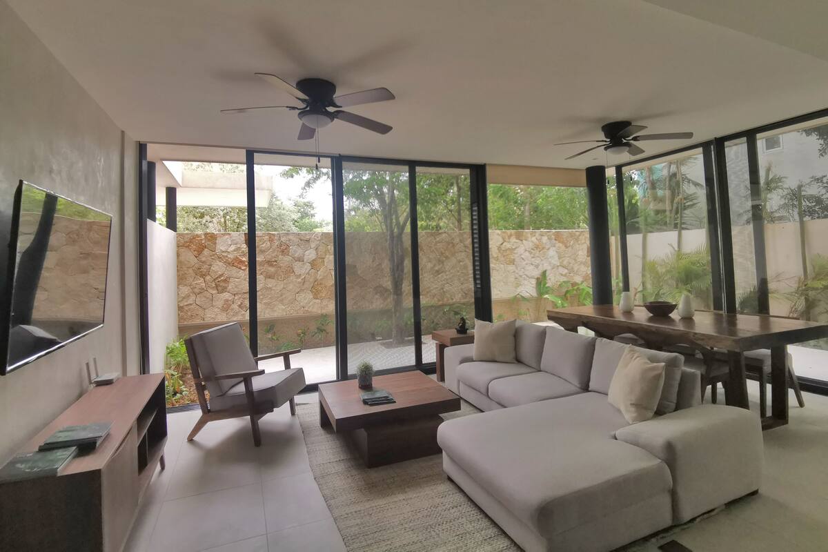 Una sala moderna con sofá, mesa de centro y sillas, televisor de pantalla plana y un comedor con mesa y sillas.
