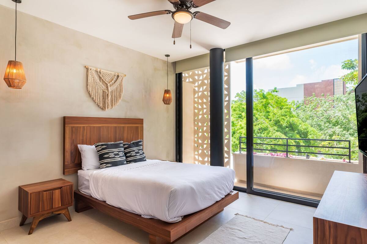 Un dormitorio moderno con una cama de madera, un ventilador de techo y un ventanal con vistas a zonas verdes.