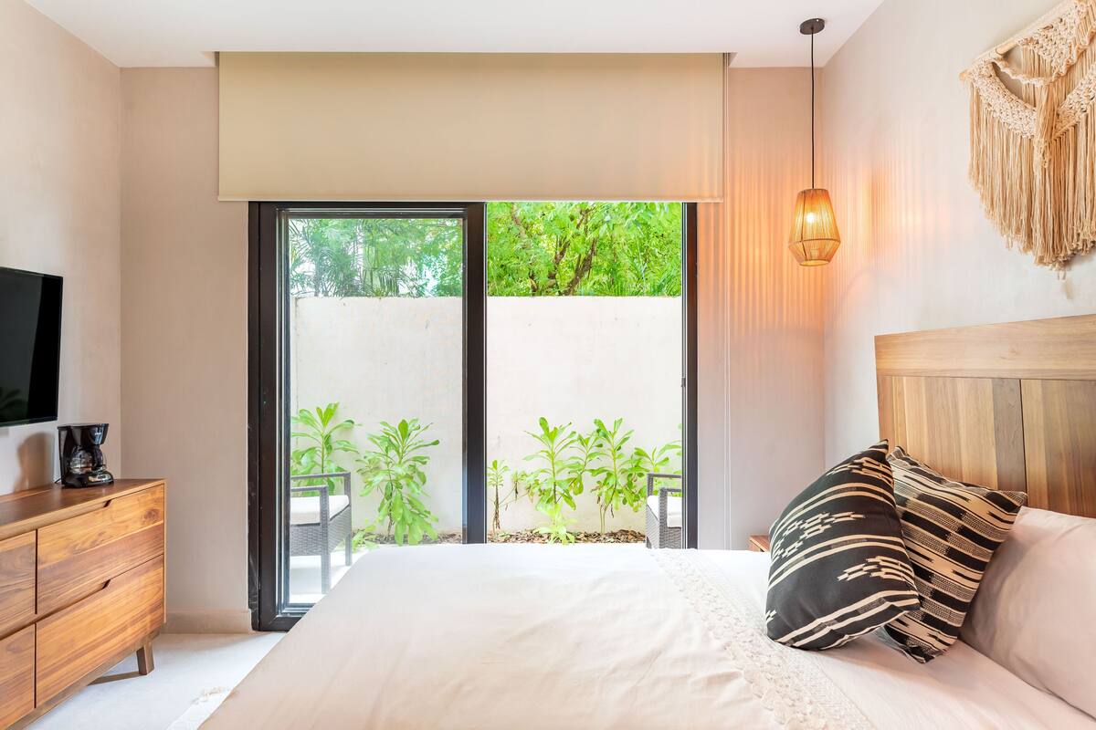 Un dormitorio con una cama, un aparador de madera, un televisor y un ventanal con vistas a zonas verdes.