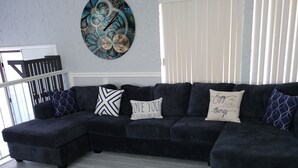 Un salon moderne avec un canapé d’angle gris foncé, une table basse blanche et un élément décoratif mural.