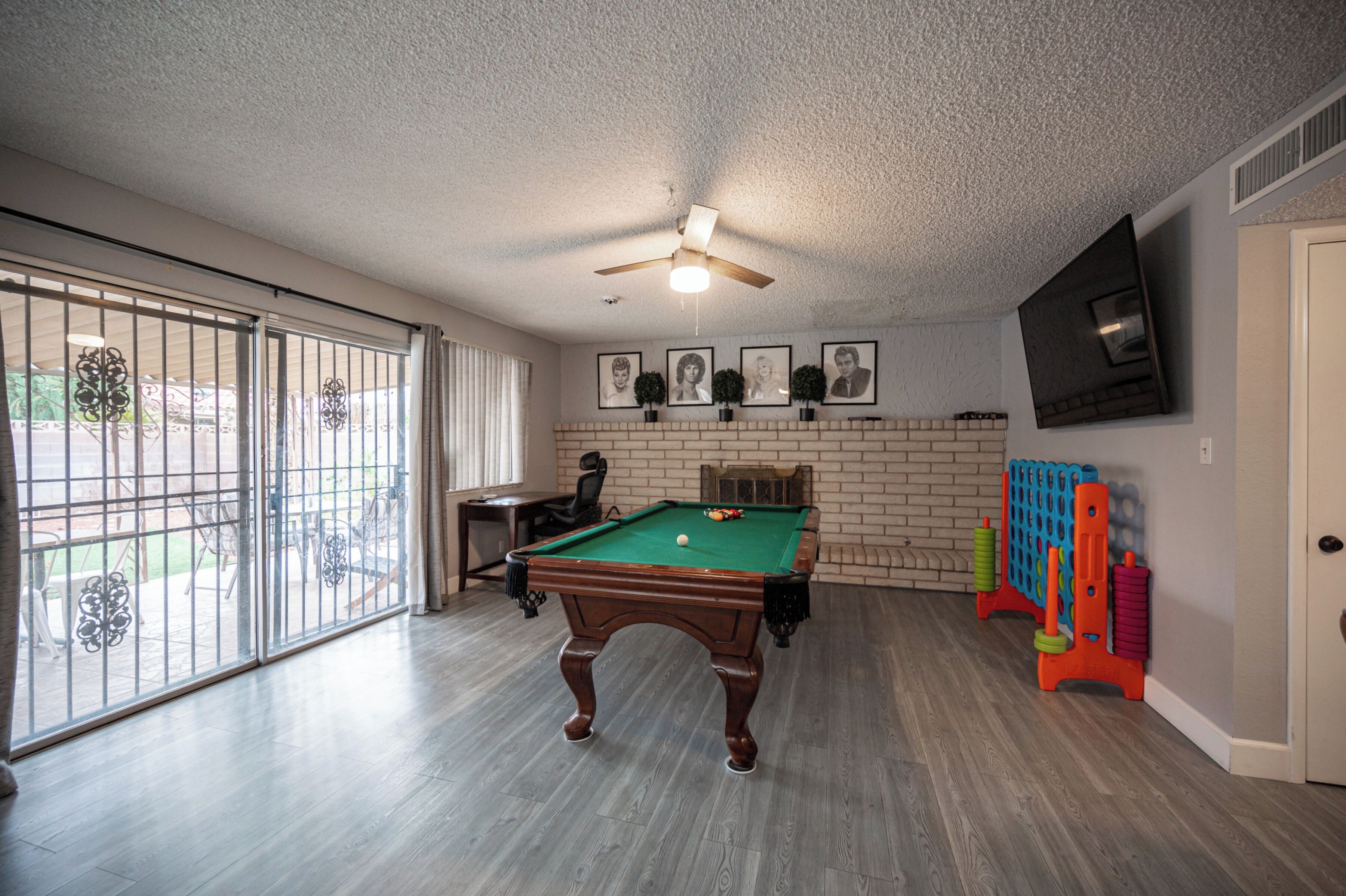 A pool table in a room with a ceiling fan, a brick fireplace, and a TV mounted on the wall.