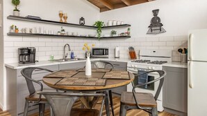 Una cocina moderna con azulejos blancos, vigas de madera, una mesa redonda y una estufa a gas.
