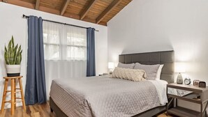 Un dormitorio con cama, mesita de noche, lámpara, reloj y planta en maceta.