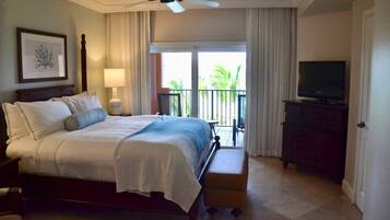 Une chambre d’hôtel équipée d’un lit, d’une télévision, d’une commode, d’un ventilateur de plafond et d’un balcon avec des rideaux.