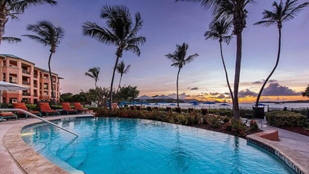 A pool with lounge chairs and palm trees, surrounded by a building with a view of the sunset. - 10% weekly disc. 2BR-Ritz-Carlton Club St. Thomas-Instant Booking- Aug 1-8, 2026 (St Thomas)