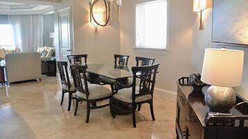 A dining area with a glass-top table and dark wooden chairs, a chandelier, and a lamp on a cabinet.