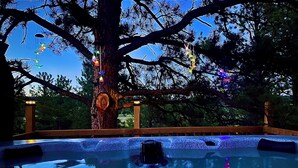 A treehouse with a hot tub, surrounded by a wooden deck and a railing.