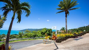 A coastal road with palm trees, a sign for 'SeaStar', and a view of the sea and mountains. - 9 Starview Apartments (Airlie Beach)