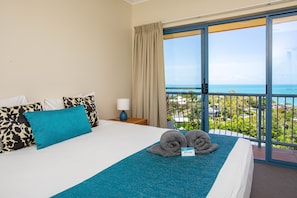 Relax in comfort with a large bed, ocean views, and a cityscape in the distance.