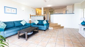 A living room with a blue sofa, a wooden coffee table, and a ceiling fan. - 9 Starview Apartments (Airlie Beach)