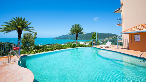 A clear blue pool with a view of the sea and mountains, a lounge chair, and a sign indicating no diving. - 9 Starview Apartments (Airlie Beach)