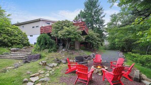 Un espace patio agrémenté de chaises Adirondack rouges, d’un foyer et d’un chemin de pierre menant à une maison.