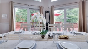 Une table à manger dressée pour quatre personnes, avec de l’argenterie blanche, des verres transparents et un centre de table composé d’orchidées blanches.