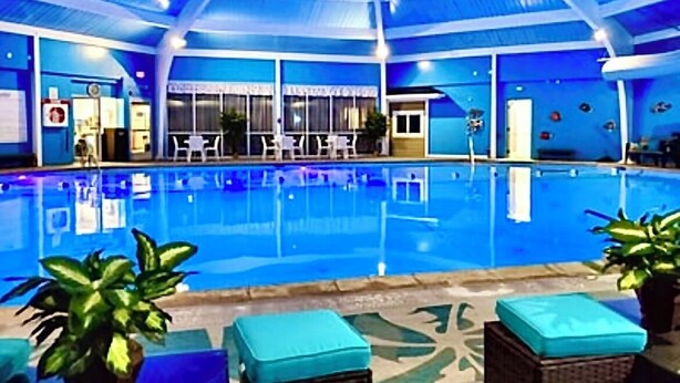 Une piscine intérieure à l’eau d’un bleu cristallin, entourée de chaises longues et de plantes en pot.