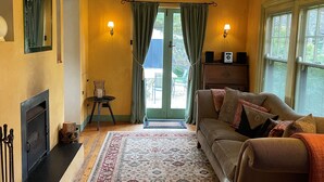 A cozy living room with a fireplace, a sofa, a patterned rug, and a view through a door.