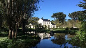 A large white house with a pond in front, surrounded by trees and greenery. - Rustic self contained cottage set in the beautiful grounds of Grayton House. (Woodend)