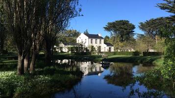 A large white house with a pond in front, surrounded by trees and greenery.