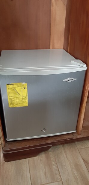 A compact refrigerator with a stainless steel exterior and white top sits on the floor.