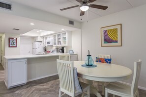 A kitchen with white cabinets, a dining area with a round table and chairs, and a ceiling fan.