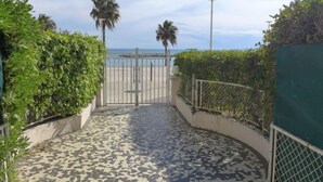 A pathway leading to a beach with a metal gate, palm trees, and a clear sky. - Le Cormoran by Interhome (Saint Laurent du Var)