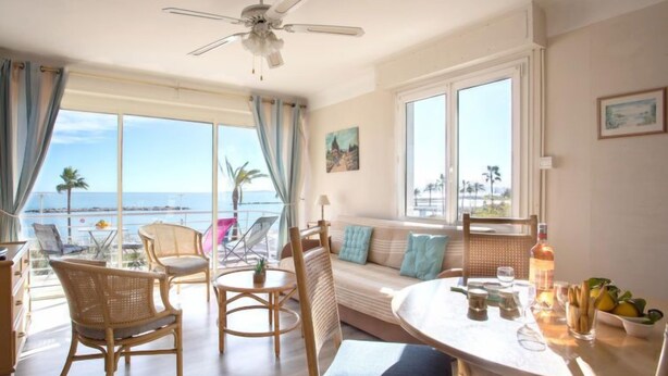A room with a balcony overlooking the sea, a ceiling fan, and a dining area with a table and chairs. - Le Cormoran by Interhome (Saint Laurent du Var)