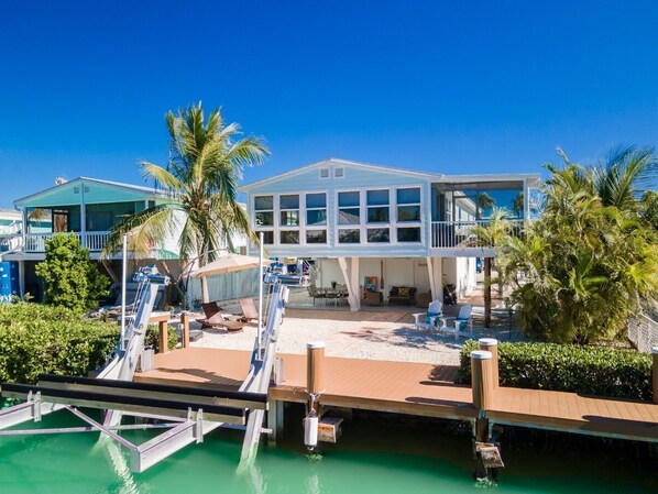 A two-story house with a balcony, a pool, and palm trees.